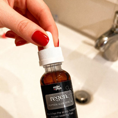 Hand holding a bottle of regen peptide hair serum over a sink.